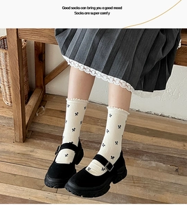 Detail of off-white crew socks with black bows and ruffle cuffs worn with Mary Janes