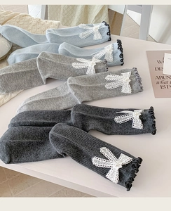Close-up of ribbed knit socks with lace bows and pearl accents in blue and grey