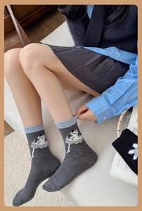 Detail of grey knitted mid-calf socks with blue ribbed cuffs and cute cartoon cat pattern