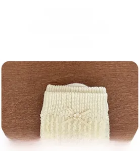 Détail chaussette en maille crème avec nœud en soie et perle sur le bord côtelé