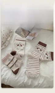 Detail showing embroidered cute puppy and cake patterns on cotton crew socks in neutral tones