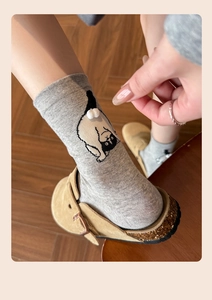 Detail of gray knitted socks with cartoon cat motif and fluffy white 3D pompom tail