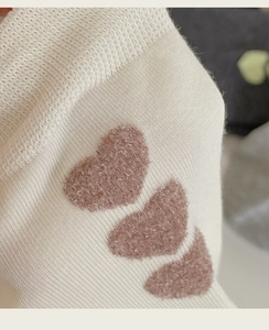 Detail of soft white cotton crew socks featuring three 3D pink flocked heart patterns