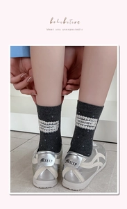 Close-up of dark grey polka dot mid-tube socks with lace brand label and silver sneakers