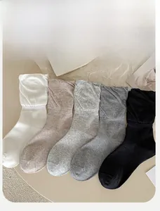 Detail of five pairs of cotton slouch socks in white, grey, and black on a minimalist desk