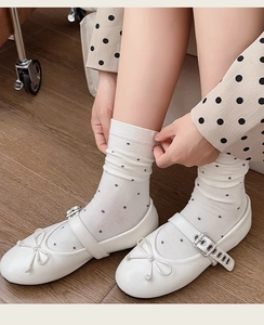 Close-up of white Mary Jane flat shoes with bow detail and polka dot cotton socks on wood floor