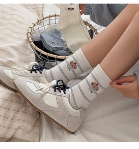 Detail of beige cotton socks with Lucky text and bear embroidery paired with sneakers