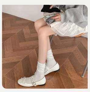 Detail showing white ruffled crew socks paired with Mary Jane shoes on a wooden floor