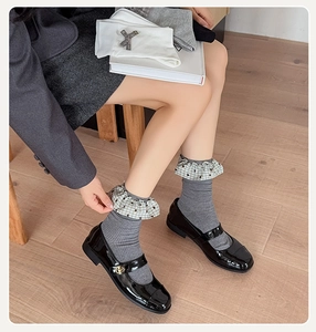 Close-up of gray ribbed crew socks with plaid ruffle trim and black Mary Jane shoes