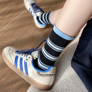 Calze a righe nero e azzurro abbinate a sneaker su un tappeto di peluche bianco