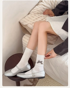 Silver Mary Jane shoes with ribbons and white ribbed socks on a wooden stool