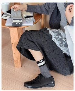 Detail of ribbed gray crew socks with striped cuff and brand tag styled with black shoes