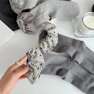 Gray rib-knit crew socks with plaid ruffle cuffs and heart detail in a cozy flat lay