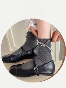 Detail of ribbed dark grey socks with ribbon bows, buttons, and ruffled cuffs