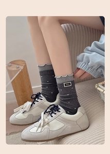 Detailed view of dark grey polka dot socks with ruffled edges and M.E.K. fabric label