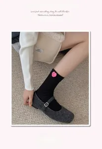 Detail of black cotton knit crew socks featuring a cute pink heart patch and elastic cuff