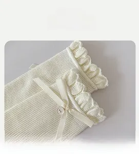 Detail view of cream ruffle socks with ribbon bow and button on elastic knit cuff