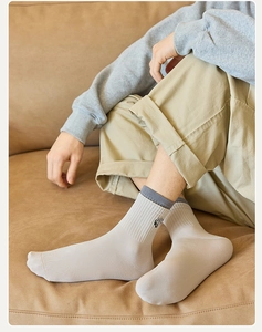 Close-up of a beige crew sock with dark embroidery and ribbed cuffs on a leather sofa