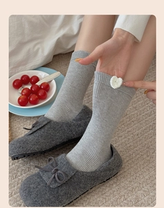 Close-up of gray ribbed knit socks with white heart detail and cozy bow slippers