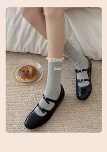 Detail of grey knitted socks with lace trim and fabric label worn with black Mary Janes