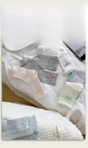 Detail of five colorful knit socks with bow decorations and ruffled lace cuffs on a white bed