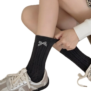 Elegant black mid-calf knitted socks with a plaid bow accent worn with sneakers