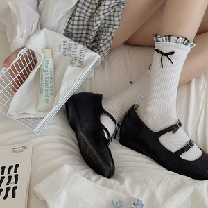 White ruffle crew socks with black bows paired with matte Mary Jane shoes on a bed