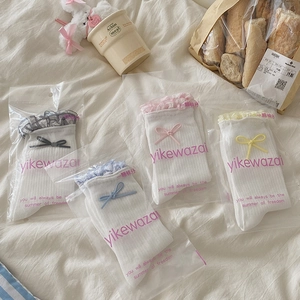 Set of four white ribbed crew socks with colorful bows and lace trim on a cozy white bedding