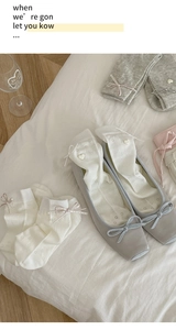 Detail of ballet style white mesh socks with ribbon bows and heart buttons with grey shoes