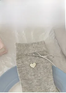 Close-up of grey ribbed socks with silver bow and miu heart button on ceramic tray