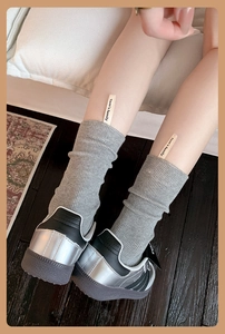 Dettaglio di calzini grigi in maglia a coste con etichetta Tom's family e sneakers con plateau