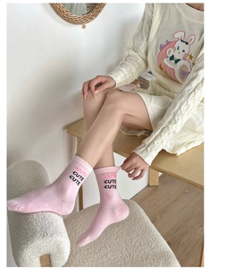 Close-up of pink socks with CUTE text paired with a white knit sweater on a model