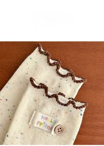 Detail of cream knit socks with colorful speckles, brown ruffle edge and letter patch