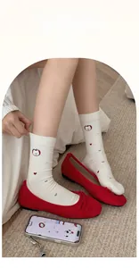 Detail of white cotton socks with apple pattern and red bow loafers in soft lighting