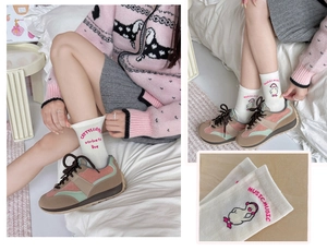 Close-up of white crew socks featuring pink letter embroidery and a cartoon duck with headphones