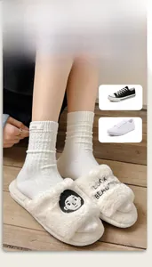 Detailed view of white cable knit crew socks with egg label and plush slippers on wood floor