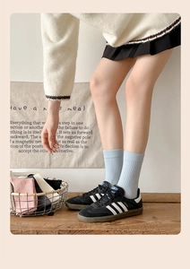 Close-up of blue striped mid-calf socks styled with classic black samba sneakers