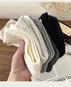 Detail of cable knit crew socks in neutral tones with minimalist egg cloth label