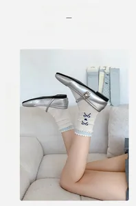 Detail von weißen Spitzensocken mit blauer Schleifenstickerei und silbernen Mary-Jane-Schuhen