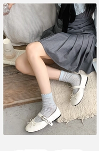 Nahaufnahme von blauen Socken mit Schleife und weißen Mary Jane Schuhen auf Holzboden