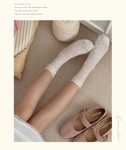 Detail of beige crew socks featuring heart patterns and white wavy lace cuffs