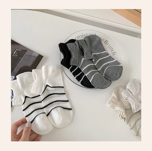 Detail of striped mesh cotton ankle socks in black, grey, and beige on white desk