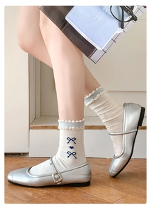 Detail von blauer Schleifenstickerei und Rüschenrand an cremefarbenen Socken mit Mary Janes