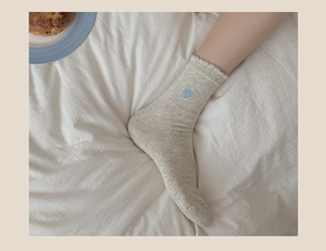 Close-up of light gray knitted socks featuring blue heart embroidery and ruffled edge