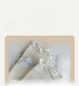 Detail of white rib-knit sock featuring elegant lettuce trim and blue plaid bow accent