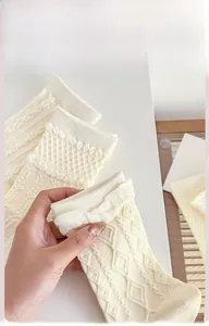 Detailaufnahmen der Strickmuster von cremefarbenen Baumwollsocken mit Rauten und Zöpfen