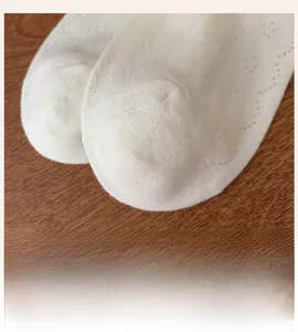 Close-up of white mesh knit socks with hollow patterns and flat toe seams on wood background
