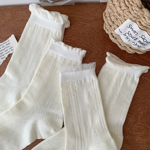Off-white lace crew socks with hollow knit patterns and ruffle cuffs on wood background
