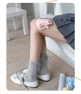 Detail of grey crew socks featuring a striped bow accent paired with white Mary Jane shoes
