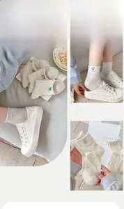Detailansicht der Bärenstickerei und bunter Noppen auf cremefarbenen Mesh-Socken